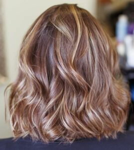 Femme brune aux cheveux bouclés bruns brillants, vue de dos dans un salon de coiffure.